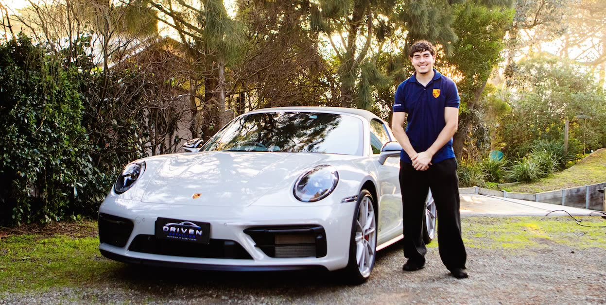 Sebastian Smith, founder of Driven Detailing, standing beside a freshly detailed white Porsche 911 with a Driven Detailing number plate